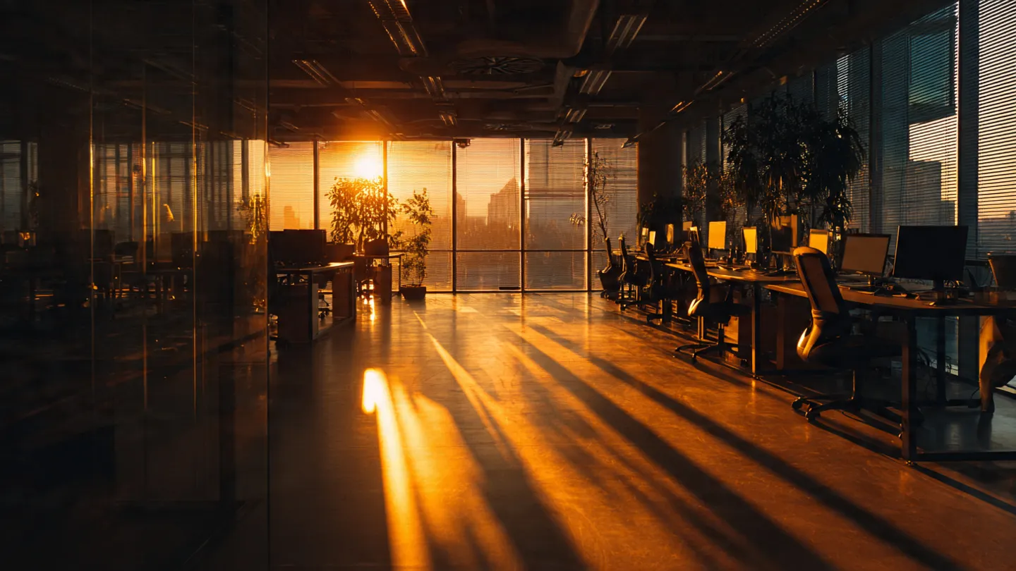 Empty modern office floor at dawn with morning light streaming through floor-to-ceiling windows